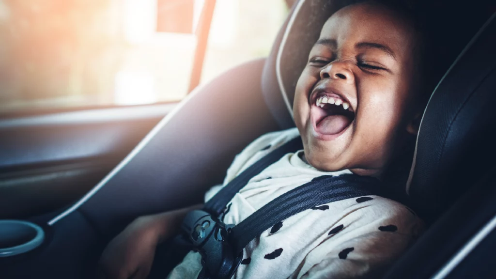 Smiling child safely seated in a luxury car seat during airport ride with New England Limo